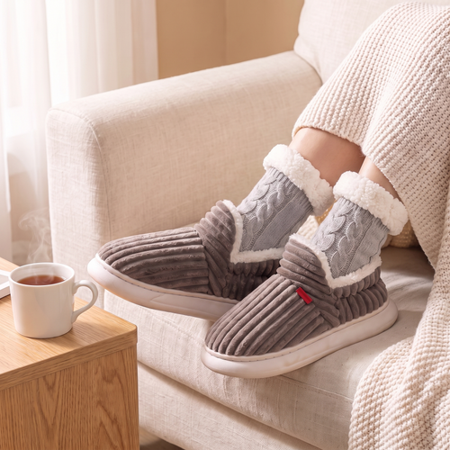 Chaussons Cocon Femme Taupe et chaussettes Torsadées Gris portés sur un canapé (vendus séparément)