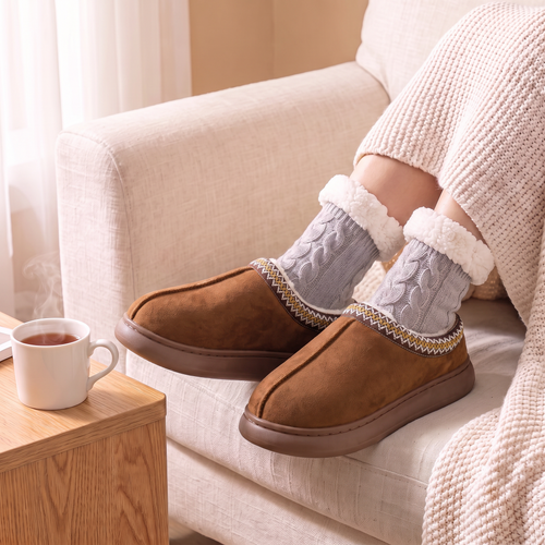 Chaussons Nordique Femme Marron portés sur un canapé, avec chaussettes Torsadées grises (vendues séparément)